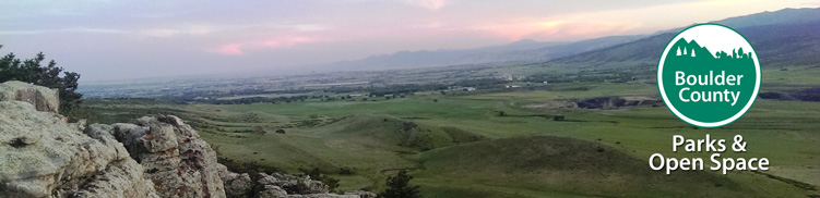 A panoramic view of green hills and valleys under a pastel sky, with a logo for Boulder County Parks & Open Space in the corner.